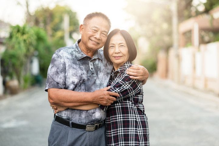 Happy elderly couple embracing each other and smiling outdoors.