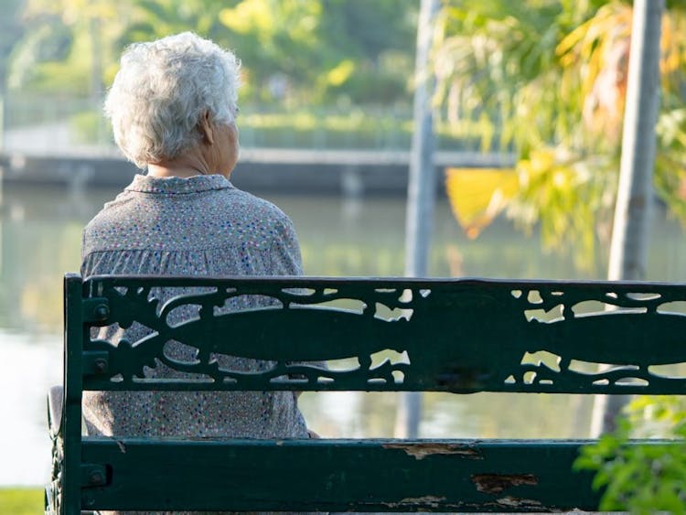 Elderly woman sitting on a park bench alone. 