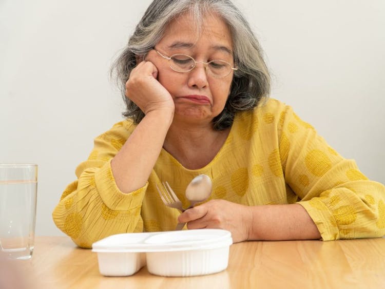 Mature woman staring at a container of food and looking sad.