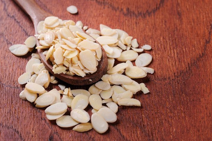 Sliced almonds on a wooden spoon and table. 