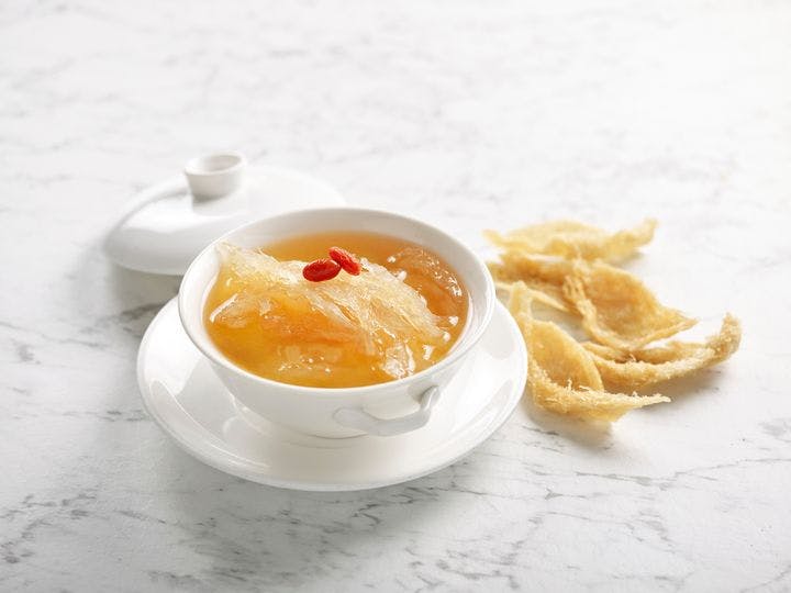 Edible bird’s nest soup in a white bowl, with uncooked edible bird’s nest pieces next to the bowl on a white marble surface. 