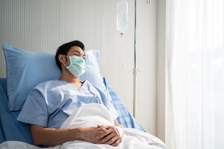 An Asian man lying on a hospital bed with a mask on