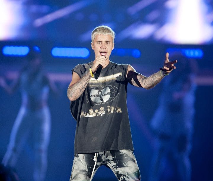 Justin Bieber backed by two dancers as he performs a song while gesturing with his left hand.
