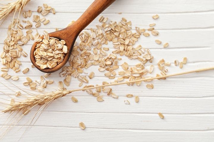 A flat-lay of oats on a wooden spoon and spread across a white wooden background.