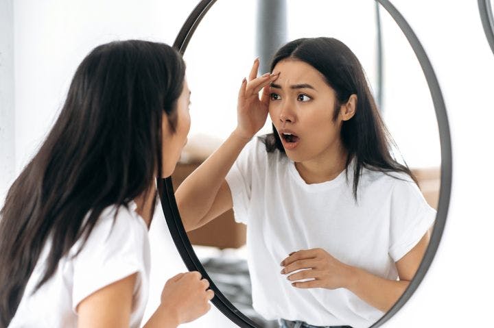 Woman with a surprise expression checking her face in the mirror. 