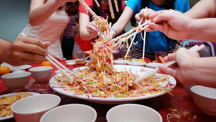 Yee sang toss in progress with yee sang platter in the middle and friends and family holding chopsticks and tossing high.
