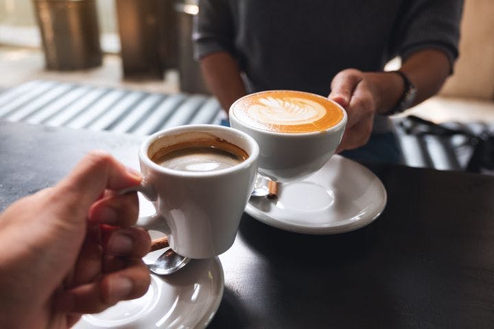 Two people clinking their coffee cups with coffee together
