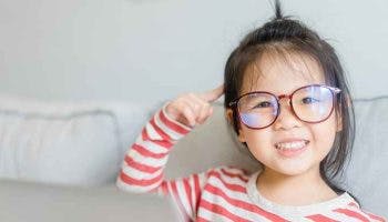 Little girl wearing glasses smiles and points to her brain.
