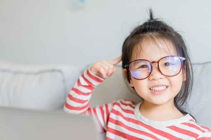 Little girl wearing glasses smiles and points to her brain.