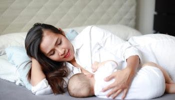 Young mother breastfeeding her newborn baby while lying on the bed.