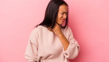 Woman with visible discomfort holding her throat with her left hand.