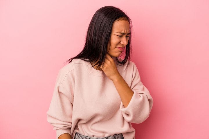 Woman with visible discomfort holding her throat with her left hand.