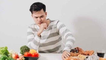 Man pushes away unhealthy high blood pressure foods placed on while table to his left, while fresh vegetables are to his right.