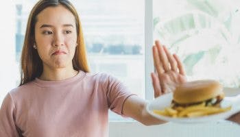 A woman with her hand held up saying no to a burger and fries.
