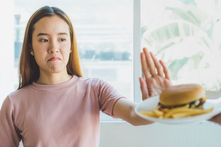 A woman with her hand held up saying no to a burger and fries.