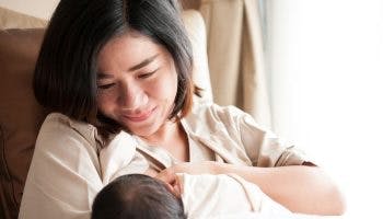 Mother breastfeeds infant while smiling and looking lovingly at her child.