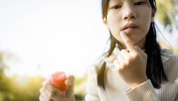 A girl touches her lip and applies ointment to heal a mouth ulcer.