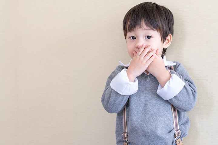 Boy closing his mouth with both hands.