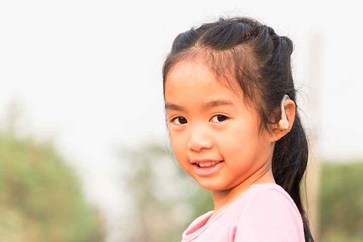 Smiling girl with hearing aid on her left ear.