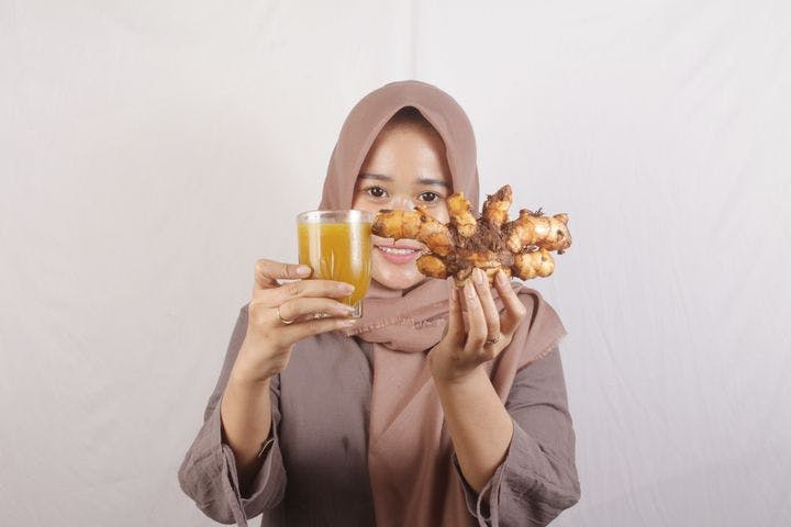 Woman holding ginger and a glass of tea.
