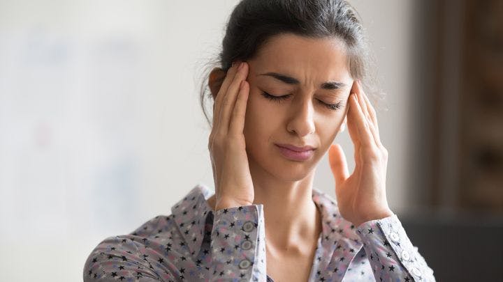 Woman is holding her forehead with two hands, experiencing postural orthostatic tachycardia syndrome (POTS) symptoms.