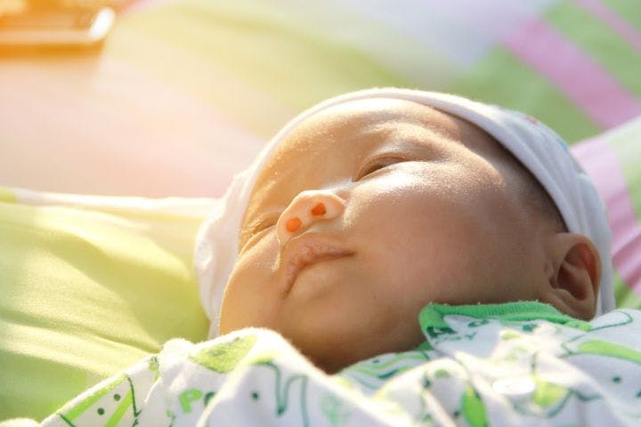 Close-up of an infant lying in bed with sunrays on her face.