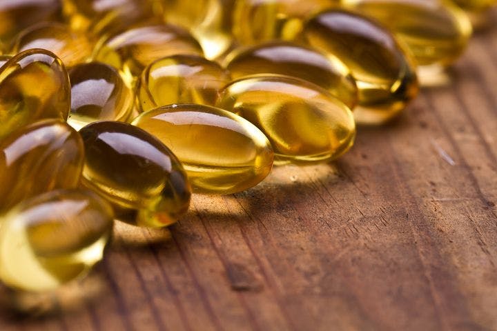 Close up shot of cod liver oil capsules on a wooden surface.