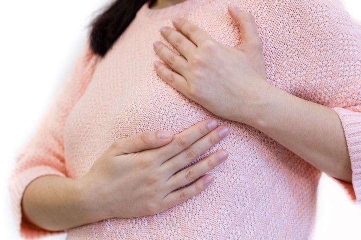 A zoomed-in shot of a woman in a pink sweater checking her breast. 