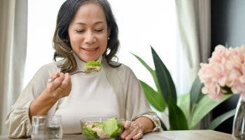 A middle-aged Asian woman eating a salad with chicken breast