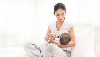 An Asian mother breastfeeding her newborn baby on a white bed.