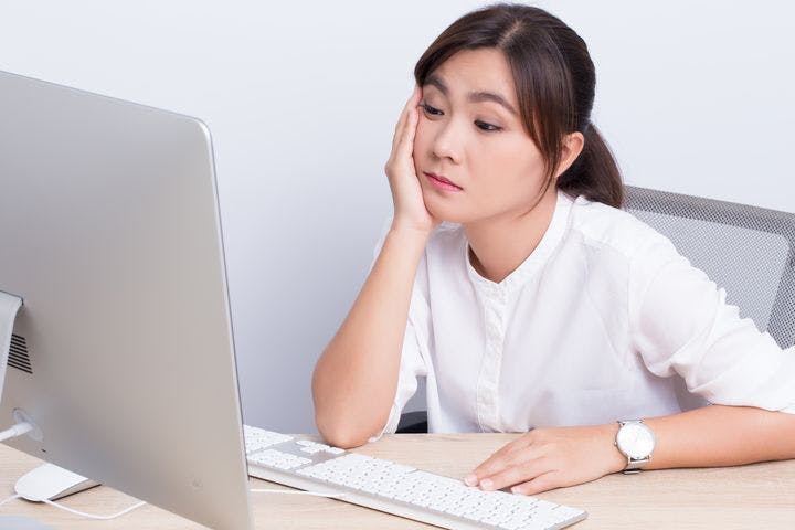 Woman looking disinterested as she stares at her desktop while sitting at an office table.