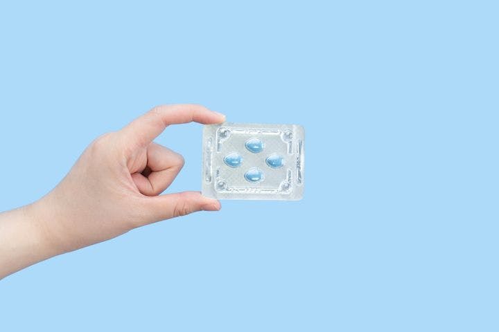Hands holding sildenafil (Viagra) pills in blister package on a blue background
