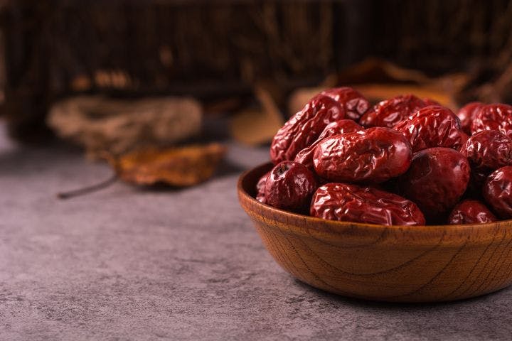Dried red dates in a wooden bowl and scattered on a table.