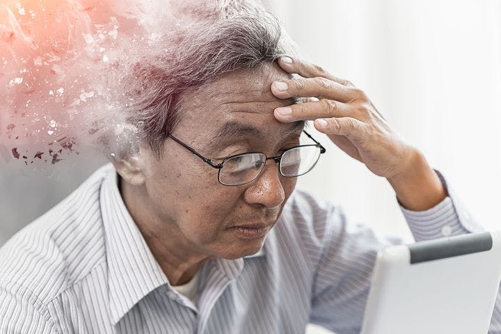 Graphic depiction of a man with Alzheimer’s disease’s head disappearing as he looks at a device while holding his forehead with his left hand.
