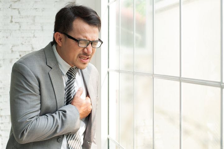 Man clutches his chest in pain, standing next to a window.