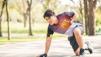Man wearing running gear kneeling on paved road while holding chest in pain.