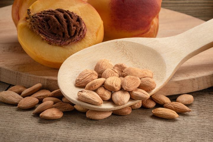 Peach kernels in wooden spoon against a background of cut peaches on a wooden surface.