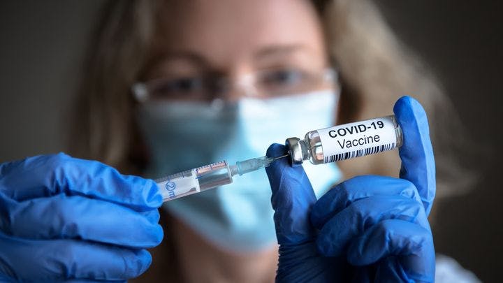 A doctor holding up a vial labelled with the COVID-19 vaccine.