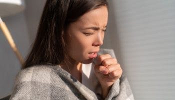 Woman coughing into her left fist.