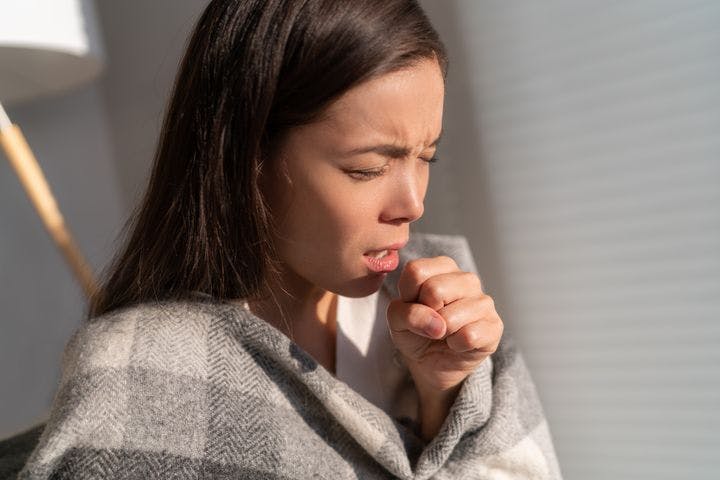 Woman coughing into her left fist.