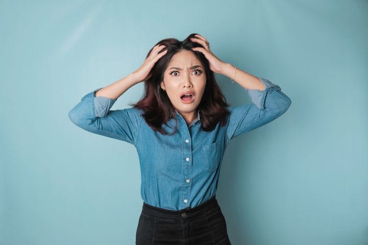 Woman with an angry expression runs her fingers through her hair in frustration against a blue background.