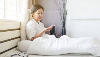 Older woman sits in bed holding a flask in one hand and pills in the other hand.