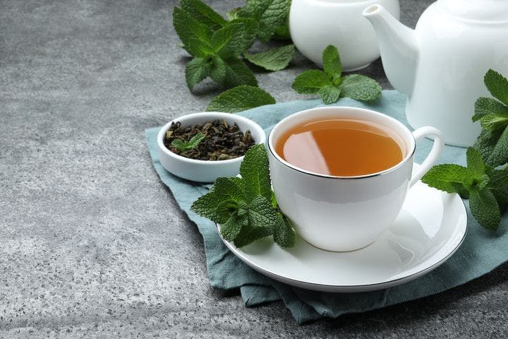 Peppermint tea in a cup with dried and fresh peppermint leaves on a saucer and surrounding it.