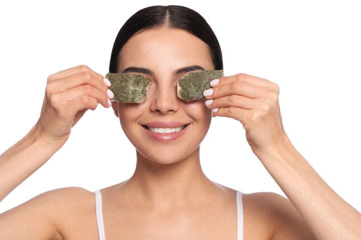 Woman holds two used tea bags over her eyes.