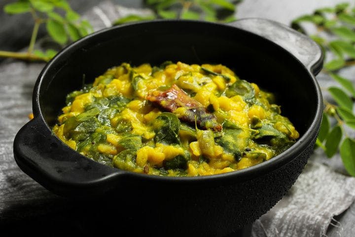 Moringa leaves cooked with lentils in a black bowl.