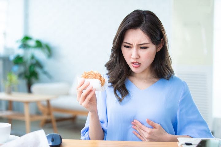 Asian woman suffers from heartburn while holding fried food.