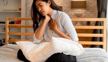 A young Asian woman holding her neck and chest while having trouble breathing. 