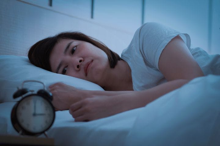 Woman lying awake in bed with a clock showing 3am.