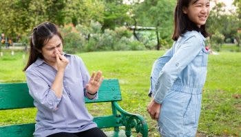 Woman covers her nose with her fingers with an expression of smelling something bad while a young girl looks embarrassed about farting.
