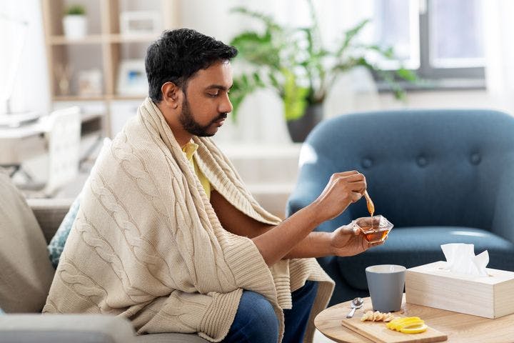 A man adding honey to his tea as a sore throat remedy